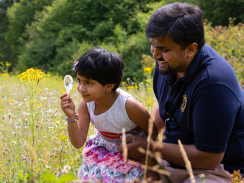 A daughter and her father in a field, using a microscope to look at an insect