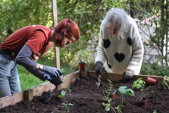 Two people planting in a raised bed using trowels 