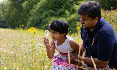 A daughter and her father in a field, using a microscope to look at an insect