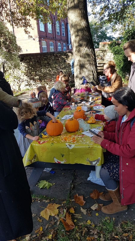 Toddlers and their parents sat at a long table, taking part in some autumnal crafts involving pumpkins and fallen leaves