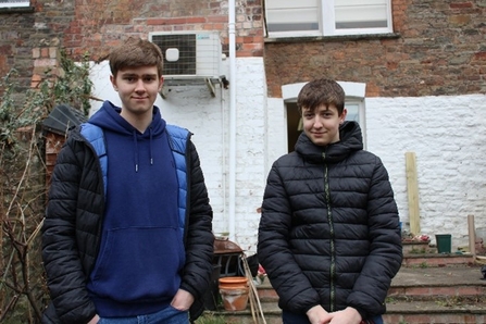 Harry and Adam stand in the garden of Great George Street and smile towards the camera