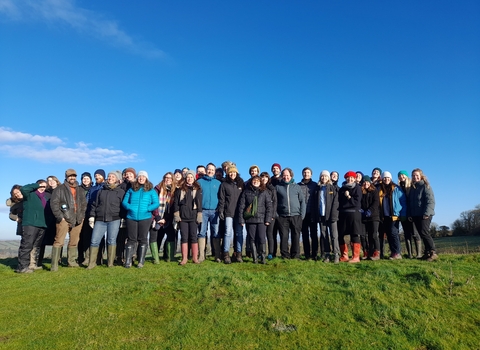 A group of Avon Willdlife Trust staff stand gathered at the top of a grass hill, with a blue sky overhead and smiles on their faces