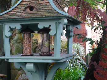 Blue bird feeder with bird seeds and fat ball not on a flat surface in a garden
