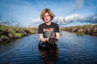 Filip stands in the water holding mud