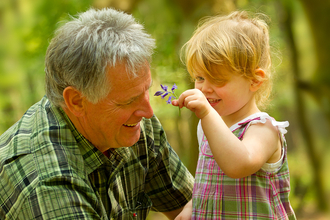 An older man next to a young child, who is holding up a flower