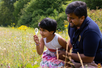 A daughter and her father in a field, using a microscope to look at an insect