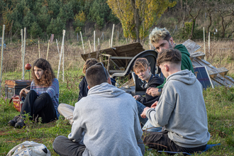 A group of young people sat in a circle, weaving willow crowns