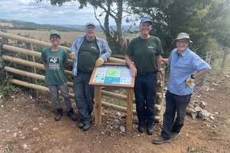 Nature reserves officer and volunteers stand either side of an interpretation board