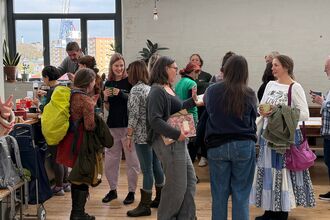 Several people gathered together talking, room has white walls and wooden floor