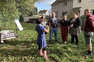 A group of nature enthusiasts stand in a circle on a local green