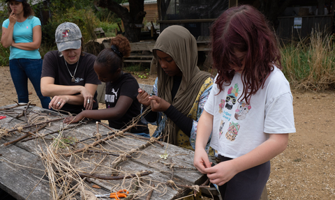 Children completing a craft activity at Grow Wilder in Bristol. Three children are sat with an adult who is demonstrating the activity