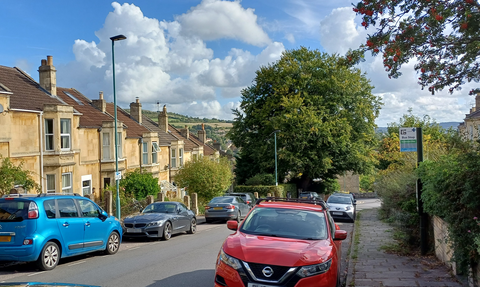 Urban street with cars, trees, blue sky with white clouds on sunny day