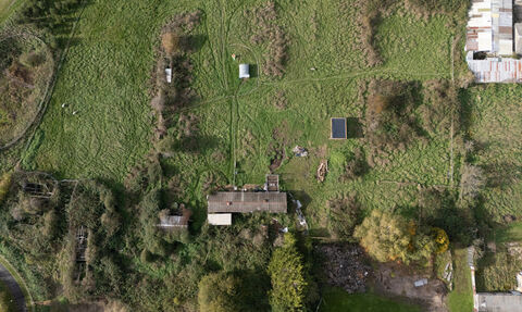 A photo taken by a drone of the land at Green Shoots, a large grassland with patches of trees and bushes, and 3 large buildings visible
