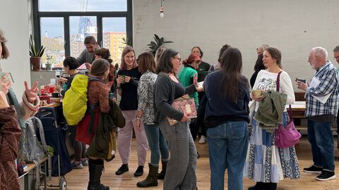Several people gathered together talking, room has white walls and wooden floor
