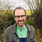 A head and shoulders photo of Christian, stood in a woodland area