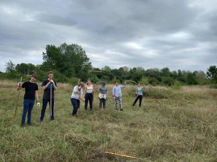 Young volunteers stood in a field with scythes