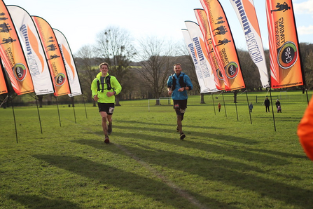 Two people running across a field, towards the camera