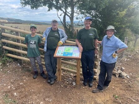 Nature reserves officer and volunteers stand either side of an interpretation board