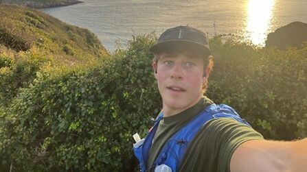 Alfie stops on a run to take a selfie, with the sun setting on the sea behind