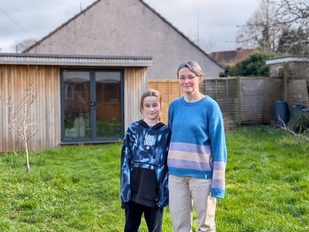 A mother and son in a garden with grass and a shed