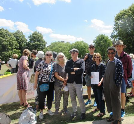 A group of older people stand together in the park on a sunny day