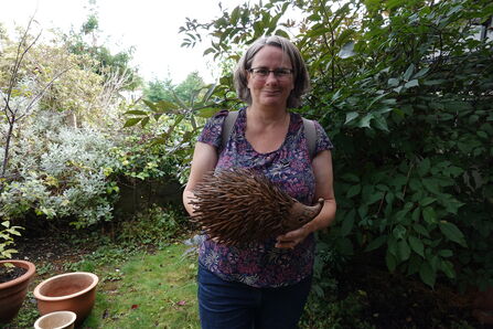 Emma stands in her wildlife garden, holding a wooden hedgehog