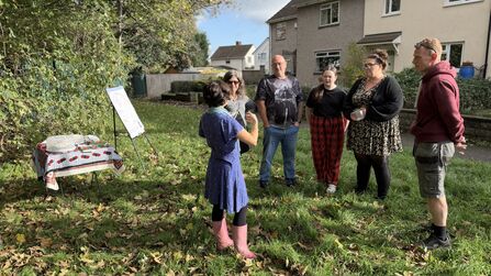 A group of nature enthusiasts stand in a circle on a local green