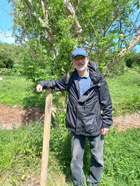Steve stands next to a fence post in a grassland area, wearing a blue cap
