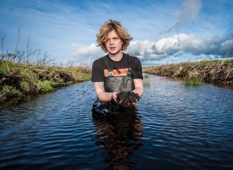 Filip stands in the water holding mud