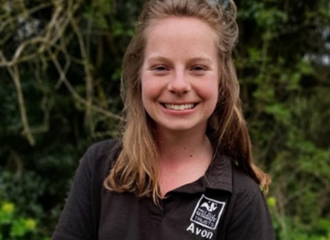 A head and shoulder shot of Esther, who is wearing a black Avon Wildlife Trust polo top. She's stood outside, smiling towards the camera with some trees and greenery behind her.