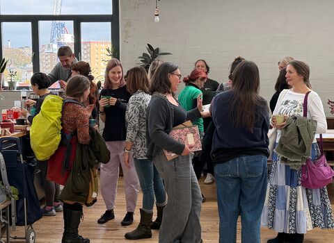 Several people gathered together talking, room has white walls and wooden floor